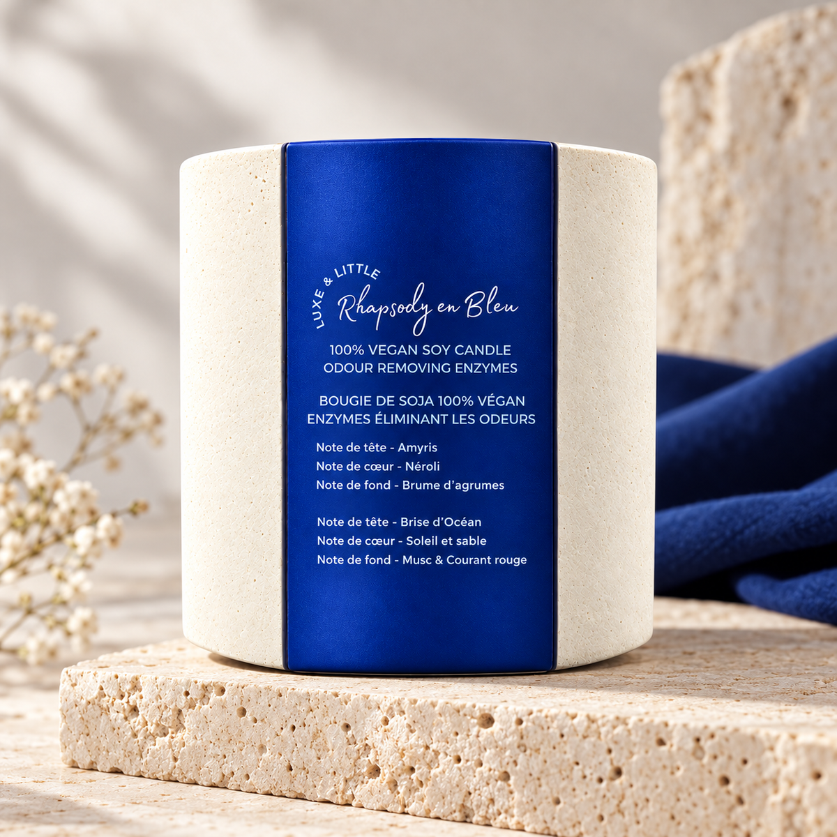 Rhapsody en Bleu unlit candle with blue wraparound label on stone beside navy linen